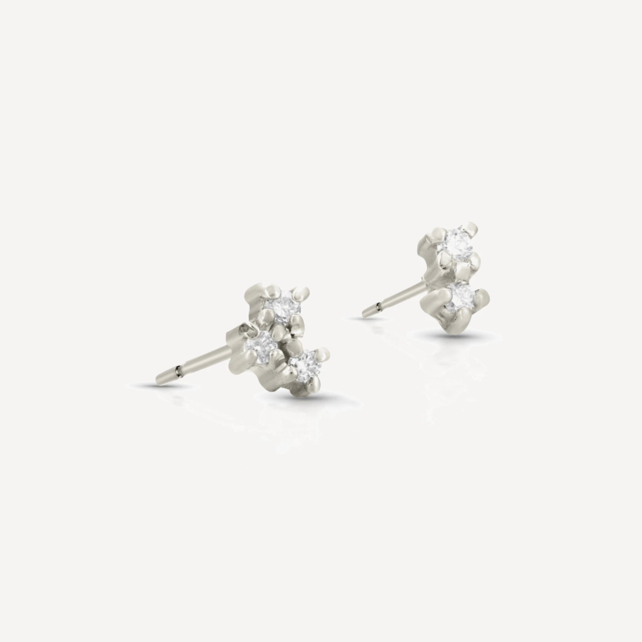 Sterling silver diamond cluster stud earrings featuring a delicate multi-stone floral cluster design with brilliant-cut diamonds on a soft beige background.