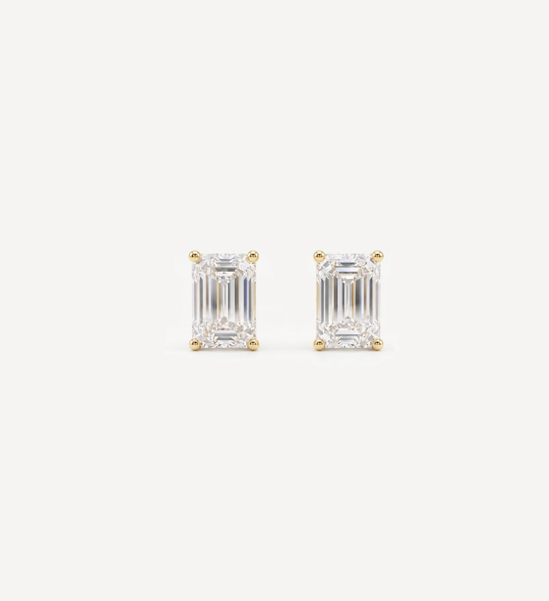 Small Emerald Grace diamond stud earrings in yellow gold featuring emerald-cut diamonds in classic four-prong settings, displayed as a matching pair